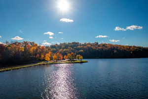 Sunburst above fall trees around the water at Cheat Lake Park