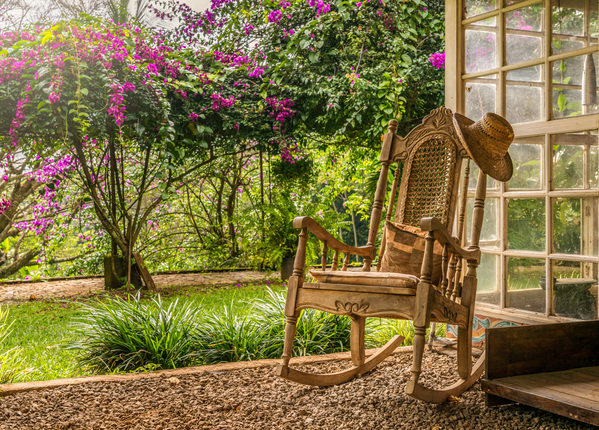 A vintage wooden rocking chair with a straw hat rests on a porch Print
