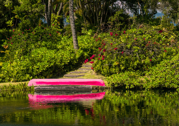 Red canoe on dock reflecting into calm lake or pond in garden by Steve Heap
