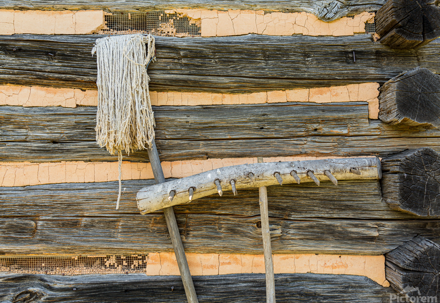 Old rake and mop against log cabin  Print