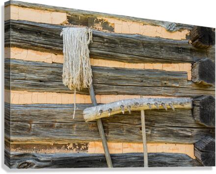 Old rake and mop against log cabin  Canvas Print