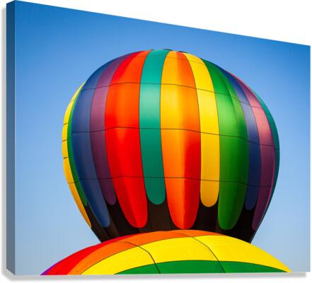 Colorful hot air balloon rising above another with blue sky  Canvas Print