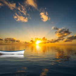 White rowing boat adrift on open ocean drifting to sunset