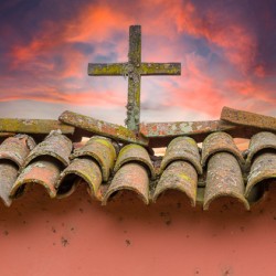 Wooden cross against brilliant sunrise at mission in California