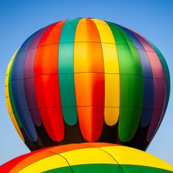 Colorful hot air balloon rising above another with blue sky