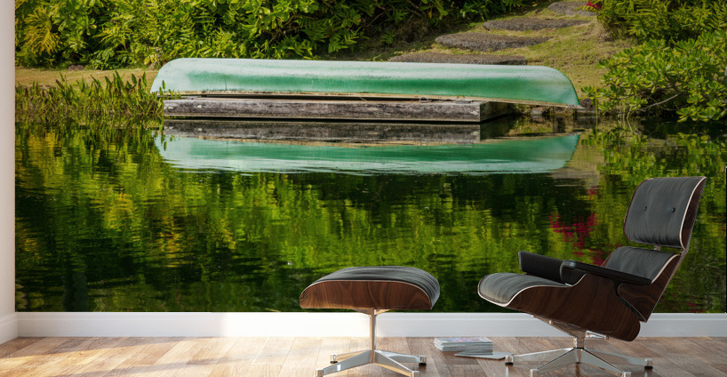 Green canoe on dock reflecting into calm lake or pond in garden Wall Murals