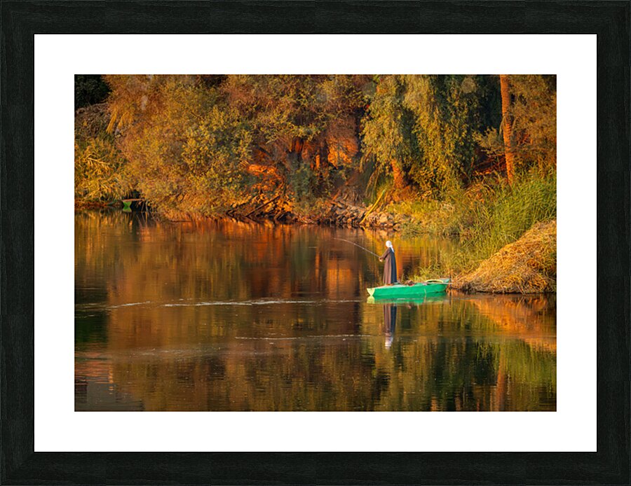 Man in traditional galabia fishing from small boat on river Nile Picture Frame print