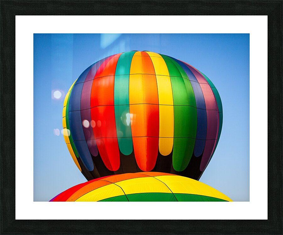 Colorful hot air balloon rising above another with blue sky  Framed Print Print