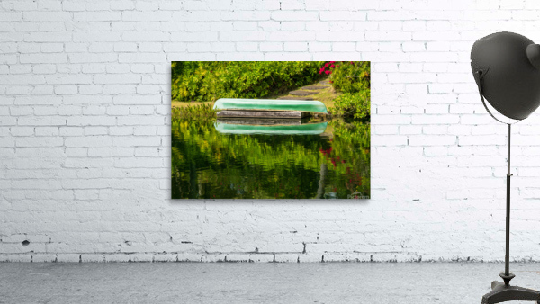 Green canoe on dock reflecting into calm lake or pond in garden by Steve Heap