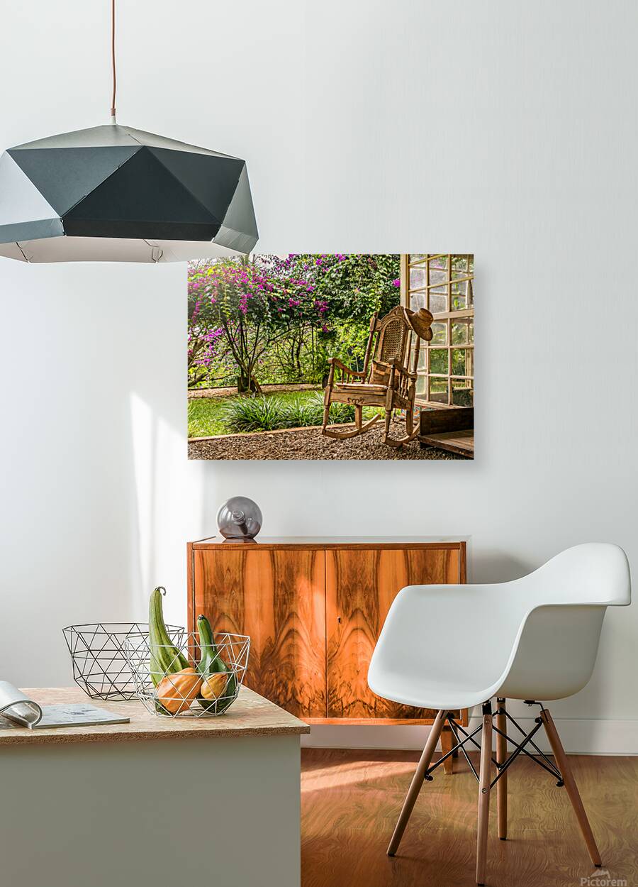 A vintage wooden rocking chair with a straw hat rests on a porch Reproduction